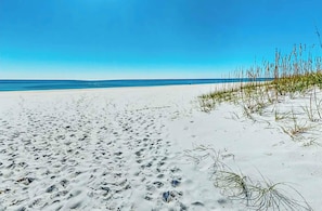A sandy beach with footprints, sparse vegetation, and a clear blue sky. - 🐚🌴Luxury 4BR Home w/ Private Elevator | Community Pool | Driftwood Dunes🌴🐚 (Pensacola)