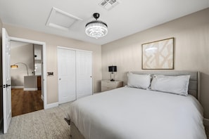 A hotel room with a large bed, a nightstand with a lamp, a ceiling fan, and a door leading to another room. - Tranquil 4-Bedroom House in charming Cave Creek-Fresh Remodel (Cave Creek)