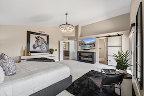 A modern bedroom with a large bed, a television, a chandelier, and a sliding door leading to a balcony. - Tranquil 4-Bedroom House in charming Cave Creek-Fresh Remodel (Cave Creek)