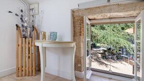 A room with a wooden floor, a white table, and a view of an outdoor area through a large window.