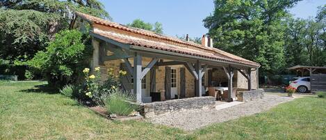 A rustic outdoor structure with a tiled roof, stone walls, and a covered patio area.