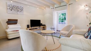 A living room with a sofa, chairs, a television, and a window with a view of greenery.