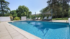 A clear swimming pool with lounge chairs and a shaded area.