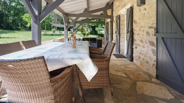 An outdoor covered patio with a dining table, wicker chairs, and a stone floor.