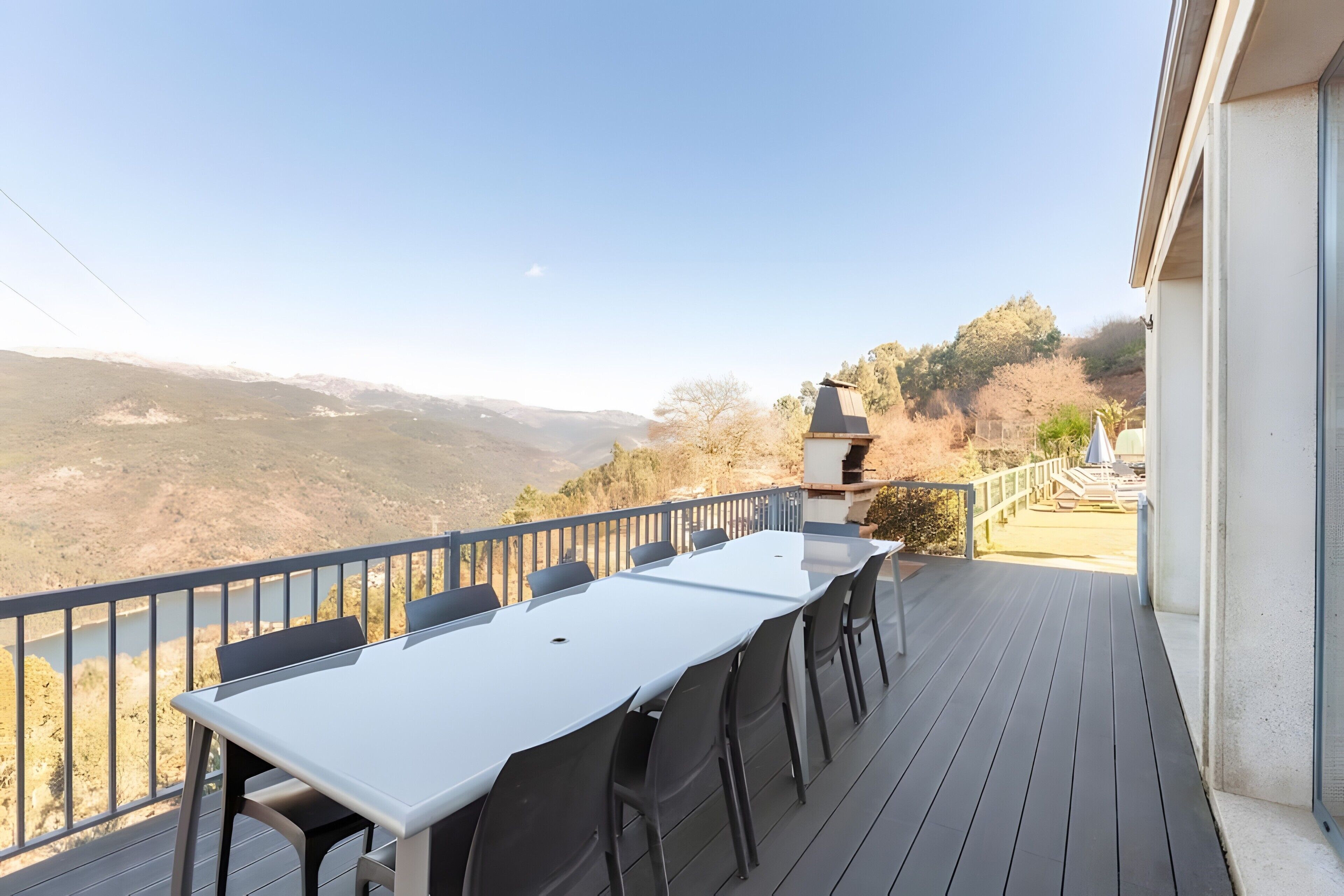 A deck with a table and chairs, overlooking a valley with mountains in the distance.