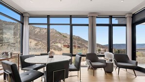 Ein stilvoller Essbereich mit rundem Tisch und Stühlen, großen Fenstern mit Blick auf die Berge und einem Balkon mit Sitzgelegenheiten.