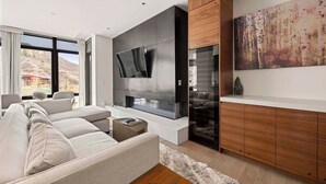 Ein modernes Wohnzimmer mit großem Flachbildfernseher, Kamin, einer Couch und einem Holzkabinett.