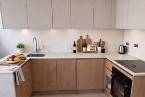 A kitchen with a sink, wooden cabinets, a countertop, a stove, and a small plant. - Contemporary 2 Bedroom Apartment (Apt B) (London)