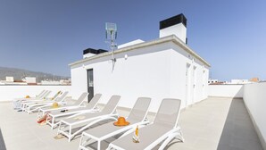 A rooftop terrace with white lounge chairs, a small table, and a bottle of drink. - Comfortable Family Stay by the Sea (Aguimes)