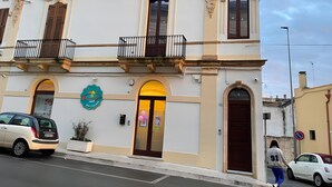 Un edificio de dos pisos con un balcón, una puerta con toldo amarillo y un letrero con un número de teléfono.