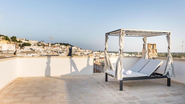 Una terraza en la azotea con una cama con dosel, vista a un paisaje urbano y cielo despejado.