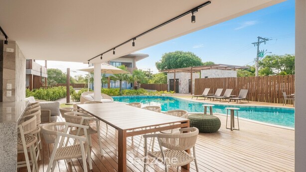 A poolside area with a wooden deck, white wicker furniture, and a view of a swimming pool.