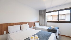 A hotel room with two beds, a window with curtains, and a view of the outside.