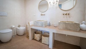 Ein Badezimmer mit Toilette, Bidet und einem Waschtisch mit zwei runden Spiegeln und einer Deckenleuchte.