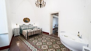 Ein Schlafzimmer mit Bett, Nachttisch, einer Kronleuchter und einem Badezimmer mit einer Badewanne.