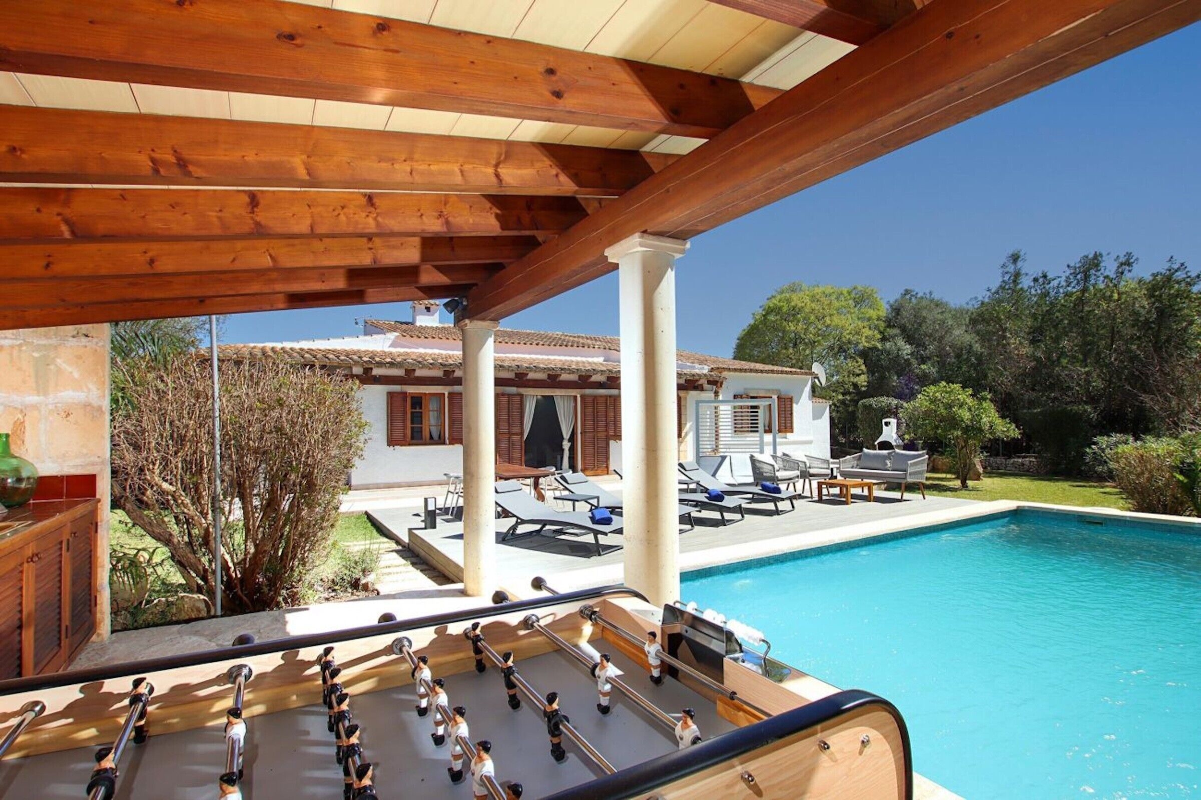 A poolside area with a foosball table, lounge chairs, and a view of a villa.