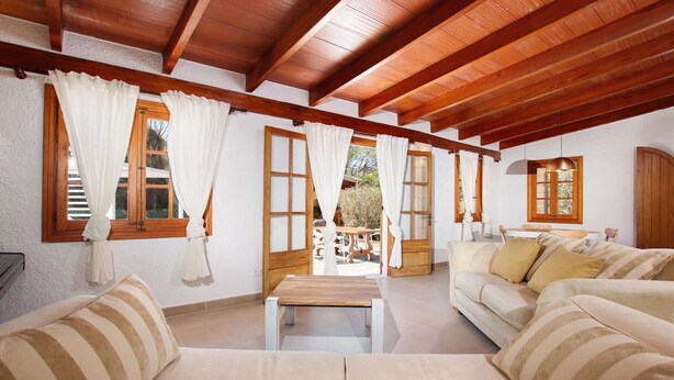 Quarto com vigas de madeira, um sofá, uma mesa e vista para o exterior.