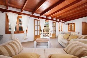 A room with wooden beams, a sofa, a table, and a view of the outdoors. - Holiday Home "Alegre" with Mountain View, Pool, Garden & Wi-Fi (Illes Balears)