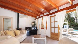Uma sala de estar com sofá, mesa de centro, TV e vista para a área da piscina.