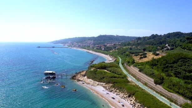 Un paisaje costero con playa, un muelle y una carretera serpenteando por las colinas.