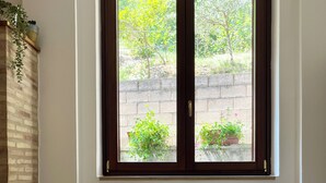 Una habitación con una mesa de madera, una ventana con vistas a zonas verdes, una pared de ladrillo y un radiador.