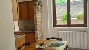 Un comedor con mesa de madera, sillas, un cuenco de fruta y vistas a un jardín a través de una ventana.