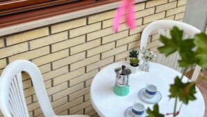 Un patio con pared de ladrillo, una ventana y una mesa con sillas y una cafetera.