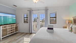 Une chambre d’hôtel dotée d’une grande télévision, d’un lit, d’un ventilateur de plafond et d’un balcon avec des rideaux.