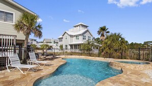 Une piscine avec des chaises longues, une maison en arrière-plan et un espace délimité par une clôture.