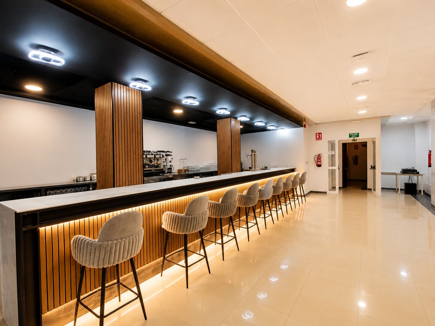 A bar area with a long counter, multiple stools, and a kitchen in the background.