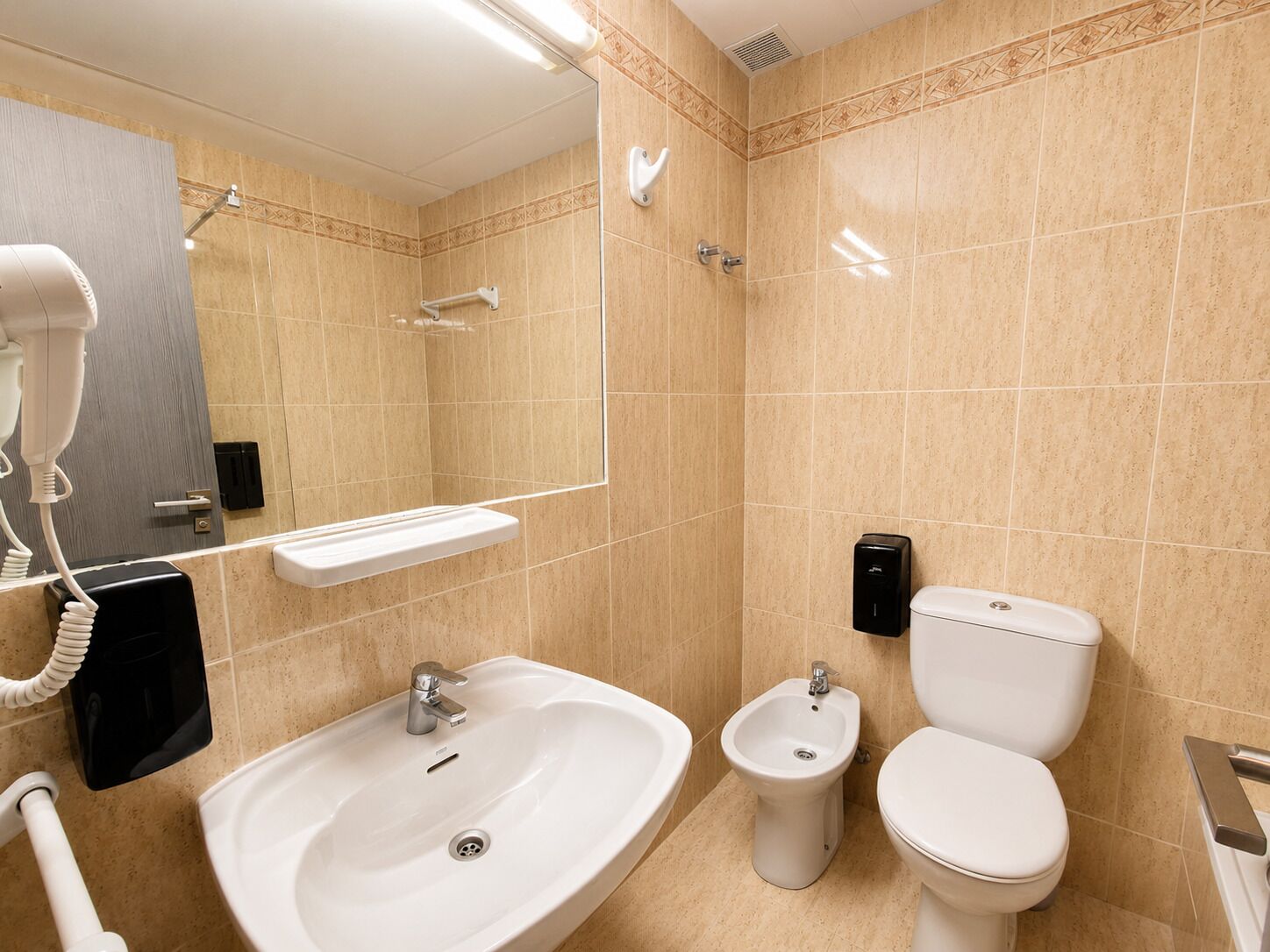 Un baño con lavabo, bidé, inodoro y secador de pelo.