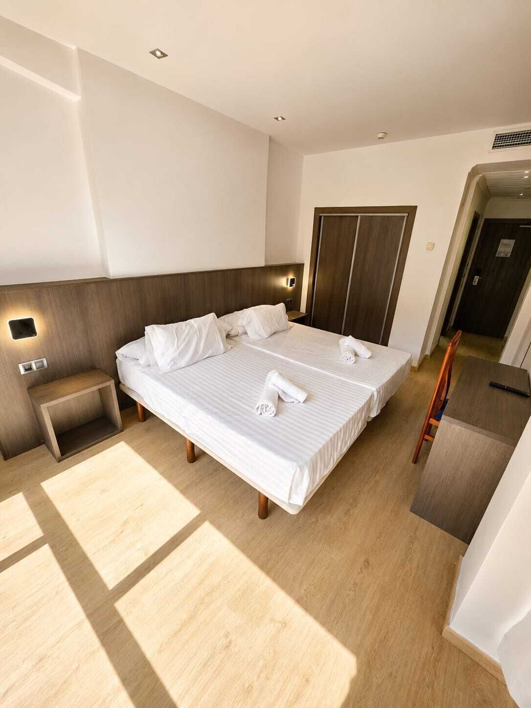 A hotel room with a large bed, bedside tables, a wardrobe, and a desk.