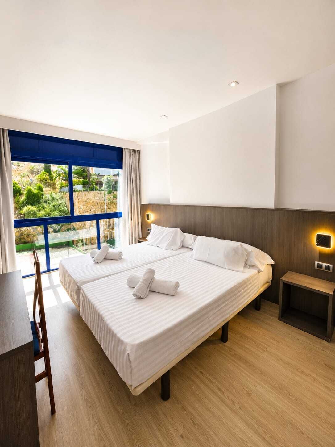 Habitación de hotel con una cama grande, un escritorio y vistas al verde exterior.