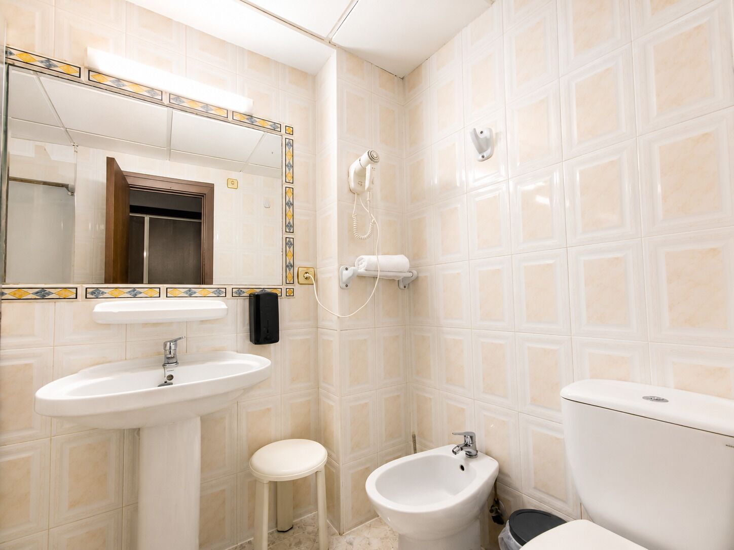 A bathroom with a sink, bidet, toilet, and a mirror with a decorative tile border.
