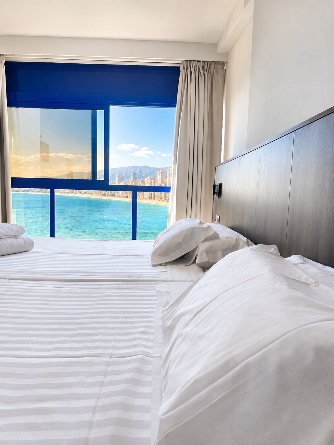 Ein Hotelzimmer mit einem großen Bett, Meerblick und Stadtansicht.