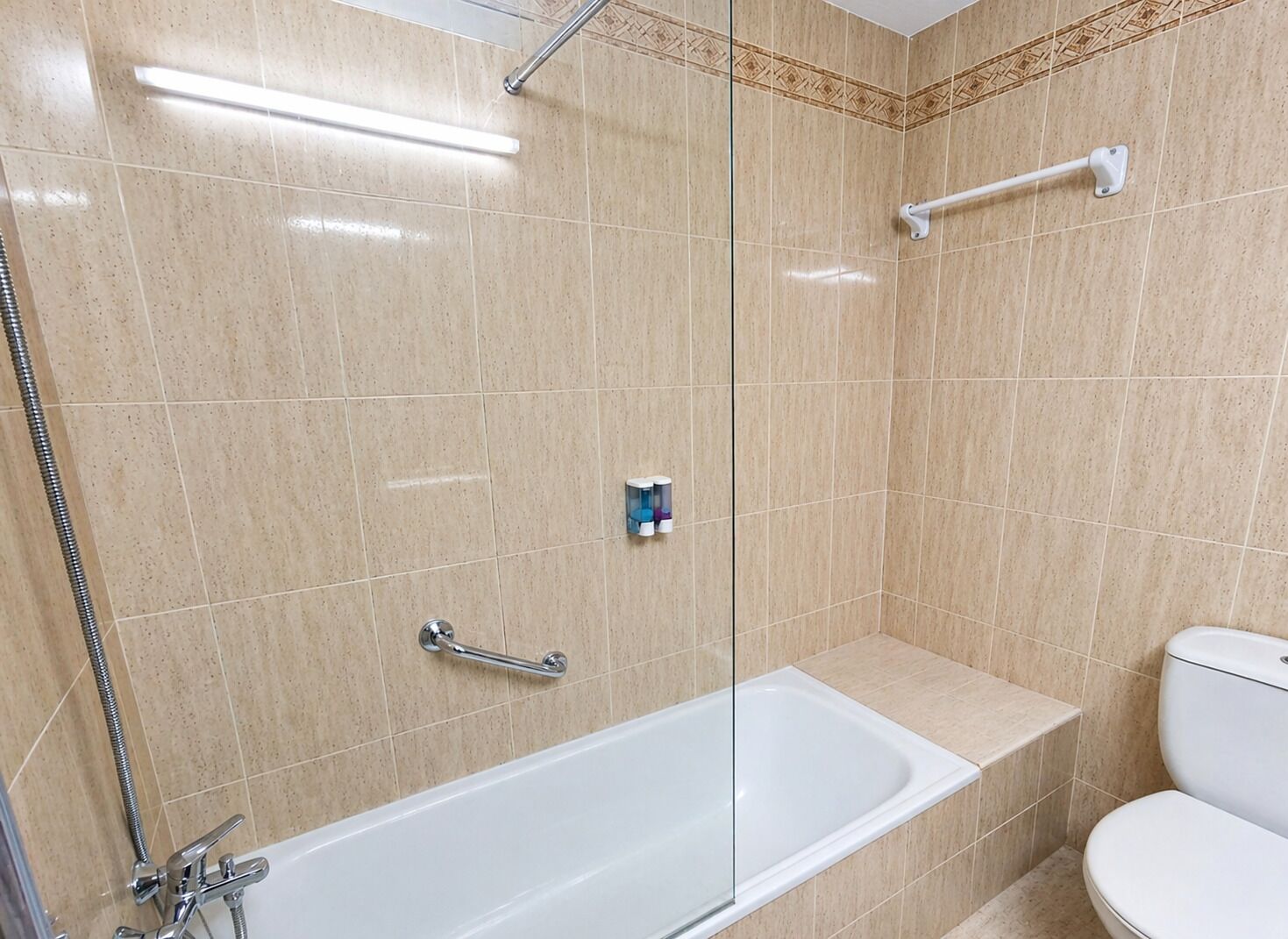 Een badkamer met een glazen douchecabine, een witte badkuip en een toilet.