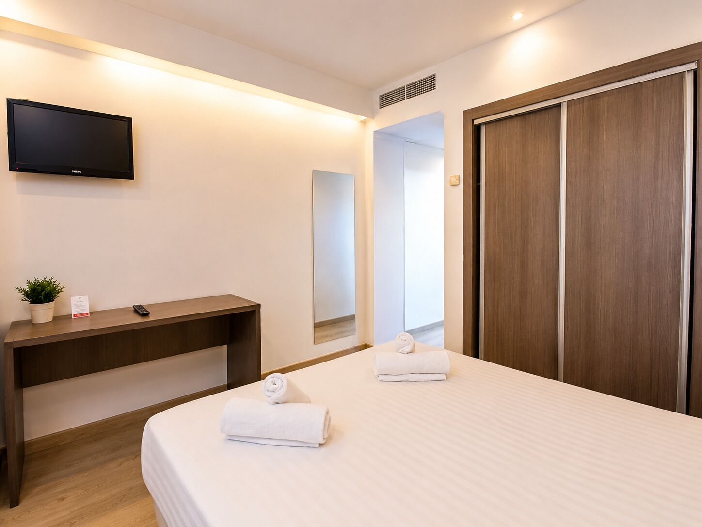 Una camera d'albergo con un letto, una scrivania, una televisione, uno specchio e un armadio.