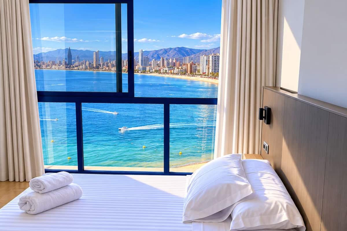 A hotel room with a large window offering a view of a city skyline and a body of water.