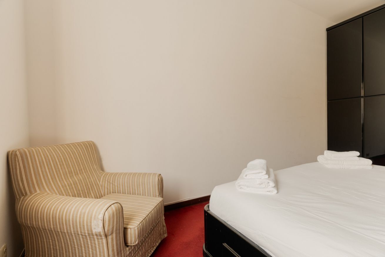 A hotel room with a bed, a striped armchair, and a black headboard.
