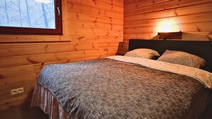 Een houten slaapkamer met een bed, een raam en een lampje aan de muur.