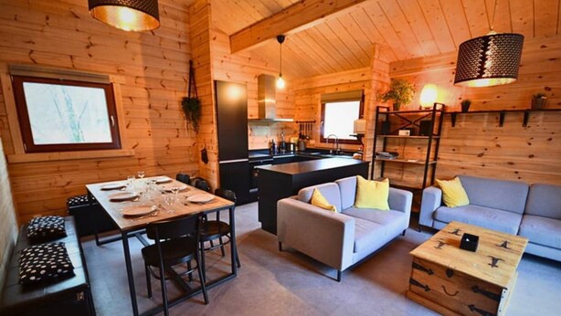 Een vakantiehuisje van hout met een eethoek, bank en een kitchenette.