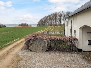 A building with a gravel driveway, a large rock, and a view of a green field and trees.