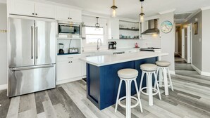 A modern kitchen with white cabinets, stainless steel appliances, a blue island, and bar stools. - Beachfront Home w/ Great Views, Private Walkover & Dog Friendly! (Galveston)