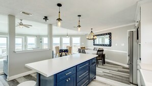 A modern kitchen with a large island, pendant lights, and a view to the outside. - Beachfront Home w/ Great Views, Private Walkover & Dog Friendly! (Galveston)