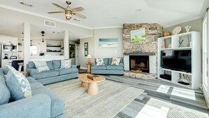 A spacious living room with a fireplace, a television, and a ceiling fan. - Beachfront Home w/ Great Views, Private Walkover & Dog Friendly! (Galveston)