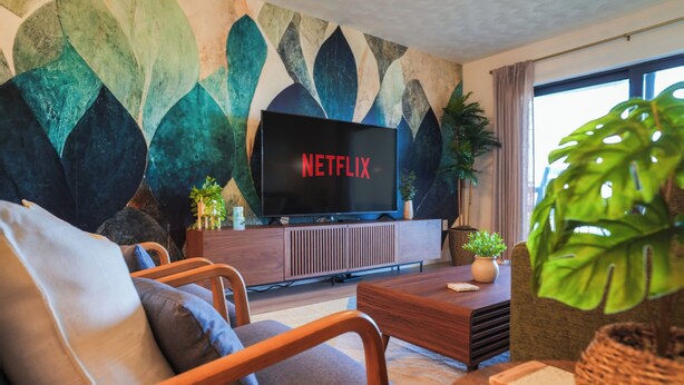 Un salon moderne doté d’un téléviseur à écran plat, de sièges confortables, d’un mur décoratif et d’une grande fenêtre.