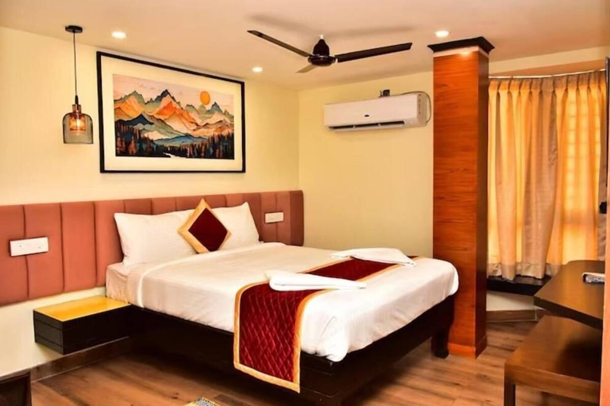 Ein Hotelzimmer mit einem Bett, einem Deckenventilator, einer Klimaanlage, einem Bild an der Wand und einem Fenster mit Vorhängen.