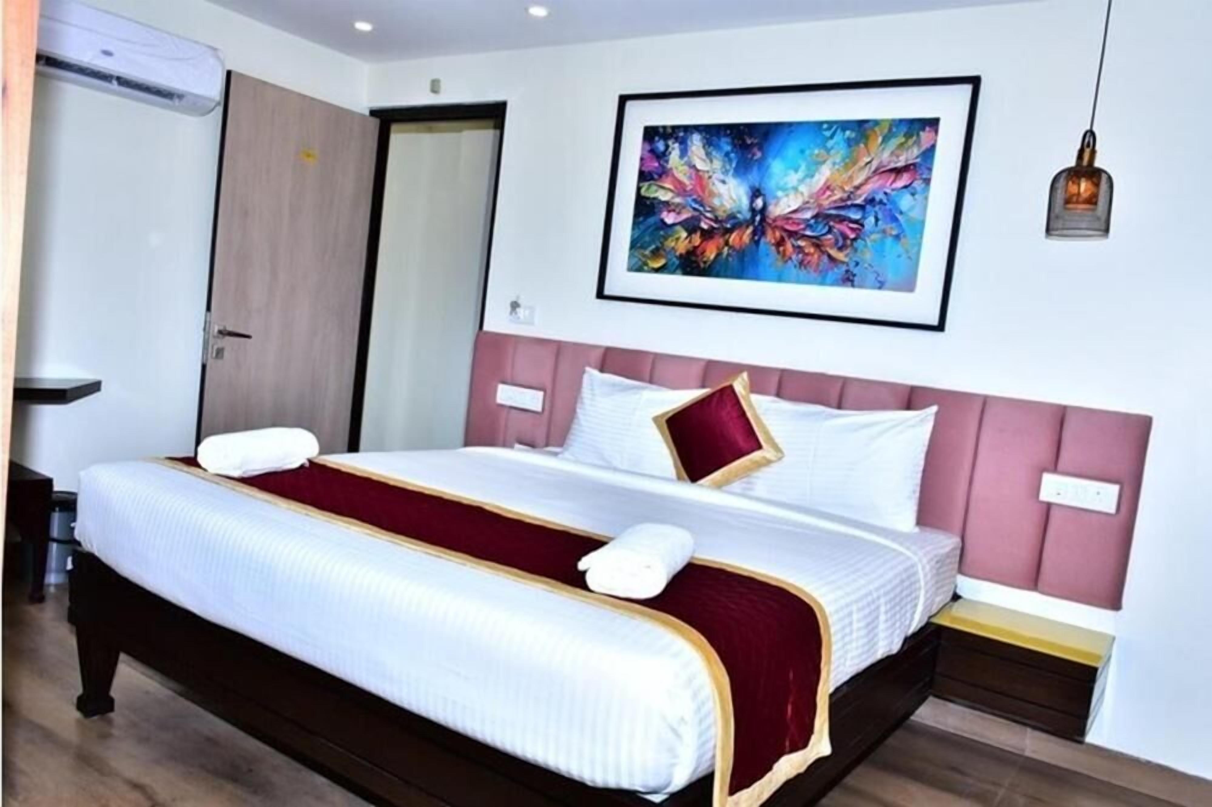 A hotel room with a bed, a painting on the wall, and a hanging light fixture.