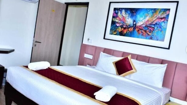 A hotel room with a bed, a wall-mounted air conditioner, a door, and a framed abstract painting. - Narayani residency (Tiruvannamalai)