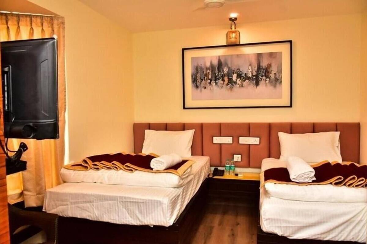 Ein Hotelzimmer mit zwei Betten, einem Fernseher, einem Bild an der Wand und einem Nachttisch mit Lampe.